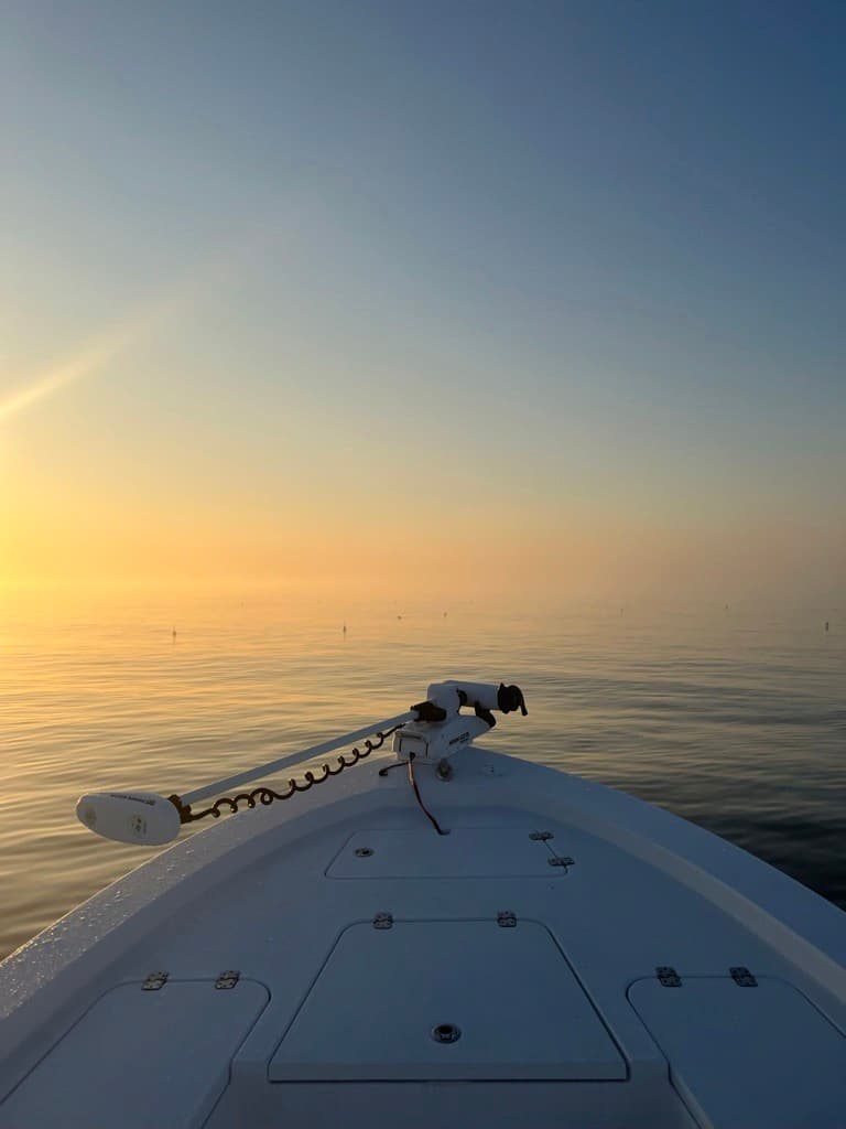 The bow of a fishing boat on calm water at sunrise