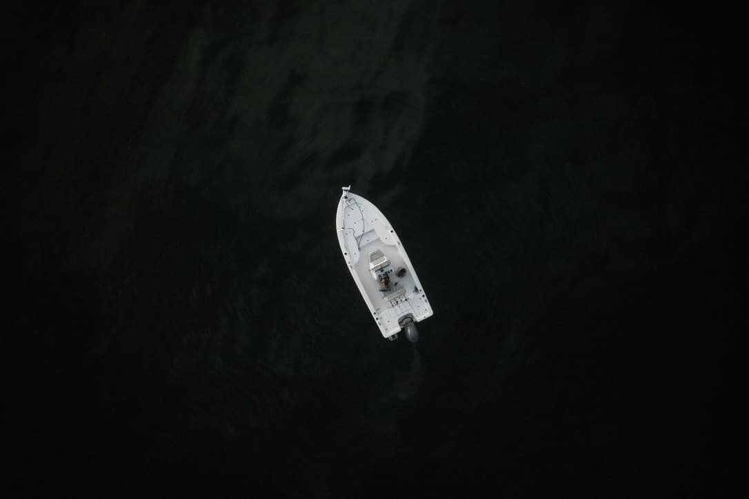 A small white fishing boat seen from above on dark water